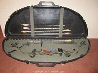 Compound bow, six arrows, and accessories inside a hard protective case with foam lining.
