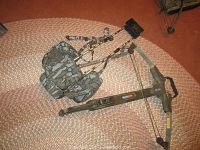 Crossbow laid next to camouflage backpack case on a woven rug, showing full size and style.