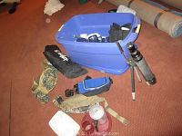 Overview of camping items including black telescope on tripod, blue plastic tote, tent storage bag, camping gloves, lantern, and other gear.