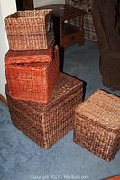 Four stacked woven baskets in different sizes and colors shown on carpeted floor near furniture.
