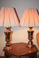 Pair of metal table lamps on a wooden side table, illuminated, showing lamp base and shade details.