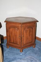Front view of Ethan Allen octagon wooden end table with closed doors showing panel detail and bun feet on carpeted floor.