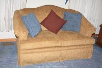 Front view of the gold-brown upholstered love seat with three pillows arranged on the seat.