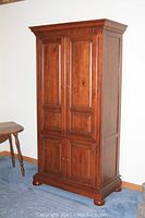 Front angled view of the closed wooden entertainment cabinet showing crown molding, paneled doors with knobs, standing on rounded feet.