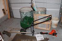 Full view of lot showing Echo weed wacker, Scotts fertilizer spreader, striped lawn umbrellas, tarps, and baby gates in garage setting.