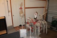 Wide view showing four white lighted wire mesh reindeer, decorative sled, and Santa mailbox stand in a garage setting.