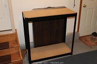 Metal and particle board storage shelf with black frame and two particle board shelves in garage setting.