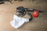 Craftsman gas leaf blower with blower tube, white catch bag, and red fuel can laid out on floor.