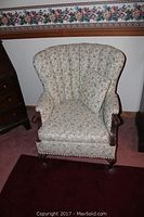 Front view of the armchair showing floral fabric upholstery, vertical tufting on the backrest and wooden frame with carved legs.
