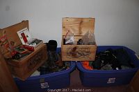 Wide view of blue storage bins filled with assorted hunting gear including boots and clothing, with two wooden carved boxes on top