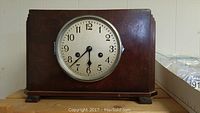 Front view of vintage wooden mantle clock with round clock face and visible wear on wood casing.