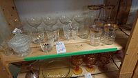 Wide view of crystal champagne glasses, pressed sugar bowls with lids and assorted clear glasses on wooden shelf