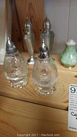Glass salt and pepper shakers with metal tops on wooden surface, part of the lot decor items.