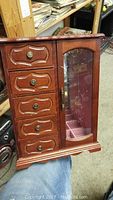 Front view of wooden jewelry box with five drawers on left and glass door on right.