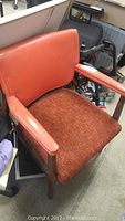 Close-up of one retro upholstered side chair showing orange vinyl backrest, wood armrests, and orange-brown textured seat cushion.