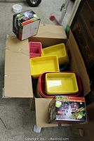 Box containing assorted plastic storage containers in yellow, red, and pink colors with two boxed cruet sets visible on top.