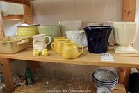 Shelf display of assorted ceramic items including mugs, vases, planters, bowls, cookware in multiple colors and styles