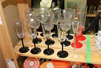 Full view of 11 stemware pieces including champagne flutes with black stems and wine glasses with matching black stems arranged on a wooden tray.