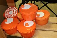 Image showing five orange plastic containers with white lids stacked together on a wooden surface.