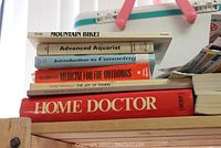 Stack of books on various outdoor and leisure topics including mountain biking, aquarist, canoeing, outdoor medicine, fishing, and home doctor guide.