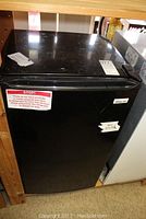 Front view of Magic Chef black bar fridge with closed door showing minor external wear and stickers.