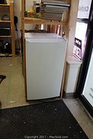 Front and top view of the white Sanyo bar fridge showing the full unit inside a room near shelves and window.