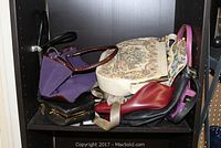 Shelf holding assorted ladies purses in different colors and styles including purple and patterned fabric purse