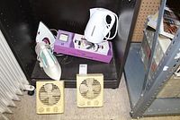 Shelving unit with two steam irons, a white electric kettle on a purple box, and two beige Seabreeze fans.
