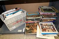 Large assortment of 33rpm vinyl records in box and stacked on shelving, showing variety of album covers and sleeves.