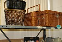 Three large wicker baskets on shelf, two picnic baskets and one single basket in various shades of brown and black