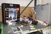 Wagner cordless drill kit and assorted tools on a metal shelf including Ryobi case, brushes, hammer, and hardware.