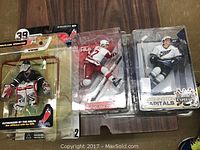 Three McFarlane Toys NHL hockey figurines in sealed blister packaging. Figurines include a goalie in black/red/white and two players in Detroit Red Wings and Washington Capitals uniforms.