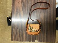 Photo of a tan handmade leather purse with butterfly motif on front flap, placed on a wooden surface.