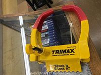 Full view of the Trimax wheel lock on a table showing yellow and red paint, branding, and the locking key engaged.