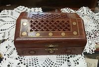 Front view of the wooden jewelry box showing brass latch, carved lid design and brass circular inlays on lid and front.