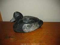 Full profile view of the wooden duck decoy on a wooden surface showing the body shape and paint wear.
