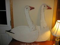 View of two large snow goose folk art wooden decoys showing side profiles, white body, orange beaks, black tail details, and metal stake stands.
