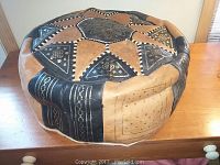 Top and side view showing the round leather patchwork design with black, tan, and brown panels and decorative motifs.