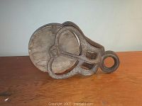 Side view of the rustic barn pulley showing the metal frame and wooden wheel resting on a wooden surface.