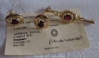 Gold tone bar pin and pierced earrings with their original identification card indicating 3.8 carat total weight of genuine garnets.