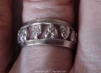Close-up photo showing vintage sterling silver ring worn on finger, displaying open heart-shaped cutout pattern around band and engraved details.