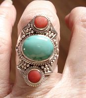 Top view of ring showing large oval turquoise cabochon and two round coral cabochons surrounded by beaded and twisted silver frame details.