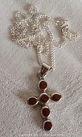 Front view of vintage sterling silver cross pendant with five oval coral stones and chain on fabric background.