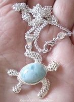 Front view of the sterling silver turtle pendant showing the oval larimar stone and chain on a hand.