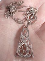 Photo showing the pendant with openwork design held in hand for size reference along with the attached chain.