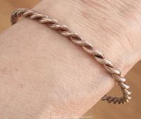 Close-up photo of the twisted sterling silver bangle worn on a wrist, showing the textured twist detail and silver tone.