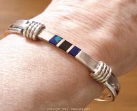 Photo of vintage sterling silver stone inlay bangle worn on wrist showing blue-green and black stones inlay, grooved band detail and polished finish.