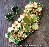 Overall view of shamrock stud earrings and bracelet with green stones on dark wood surface.