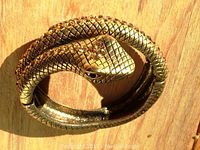 Top view of brass toned serpent bracelet showing coiled body with scale texture and inlaid topaz-colored stones.