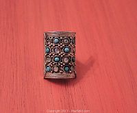 Ring on a flat wood surface showing the front face with 16 round turquoise and moonstone cabochon stones arranged in a rectangular pattern with silver beaded details.